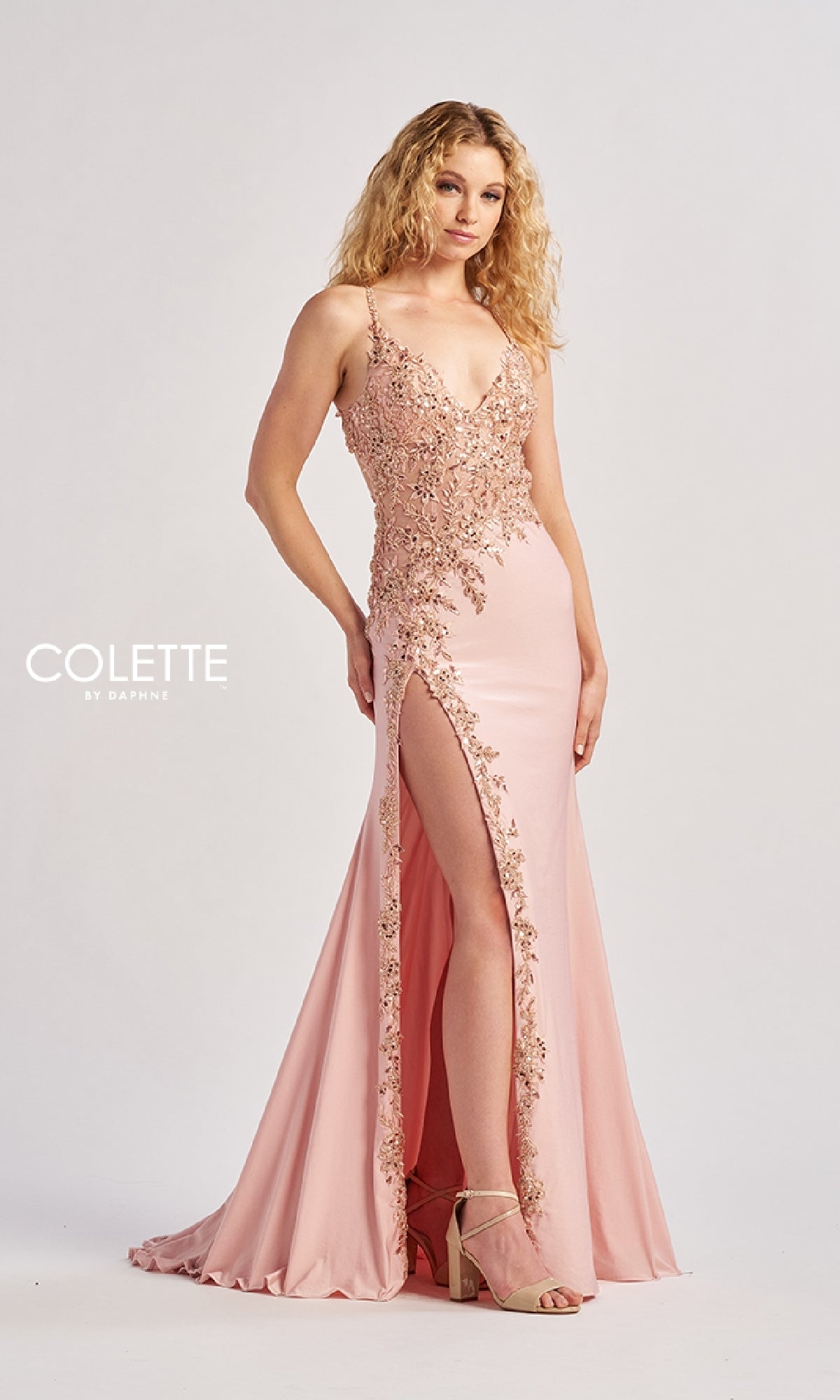 A woman wears the Colette CL8535 long prom dress—light pink with floral embellishments, lace embroidery, spaghetti straps, and a thigh-high slit—paired with high-heeled sandals against a plain background.